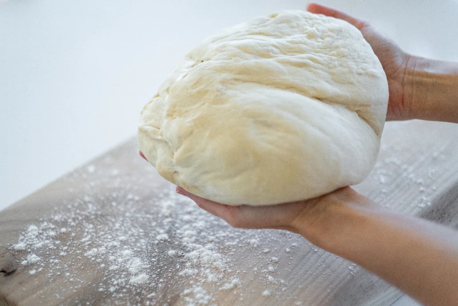 A baker's hands holding a smooth ball of dough